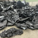 Czarne fragmenty zbiorników i zbrylone odpady z formowania tworzywa na posadzce hali