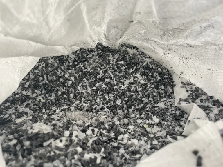 Dunkelgraues Kunststoff-Mahlgut mit helleren Flocken in einem weißen Big-Bag, Nahaufnahme